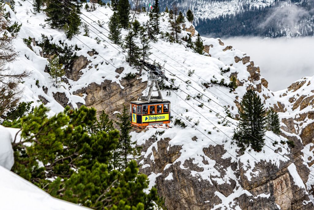 Cable car cabin climbing above snowy cliffs and pine trees in Cortina d'Ampezzo, Dolomites