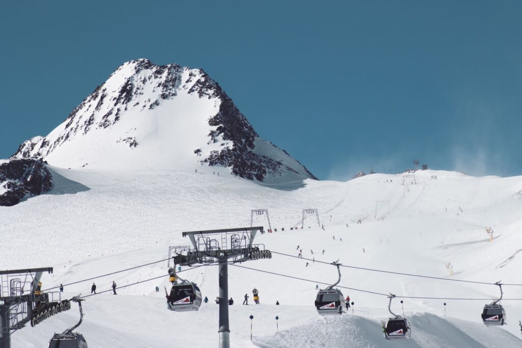 Ski gondola cabins on a cable line in front of snow-covered mountain peaks
