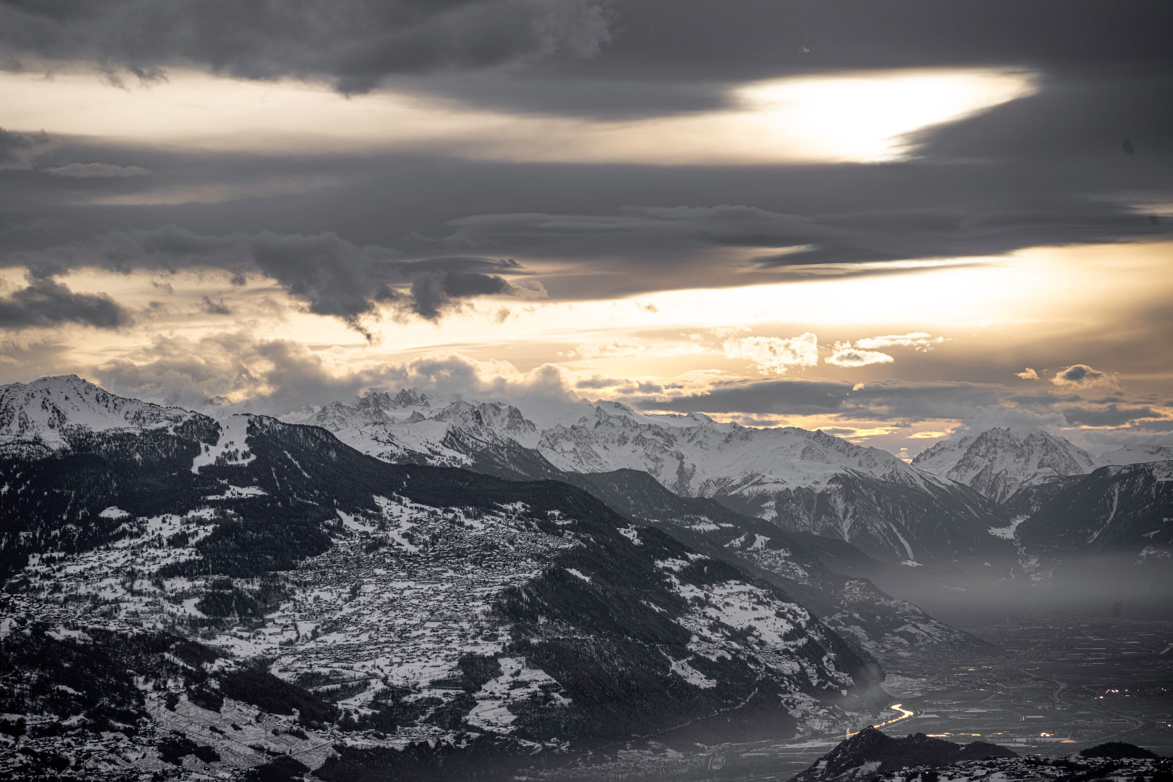 Golden sunset light breaking through clouds over the snow-capped Swiss Alps above Crans-Montana