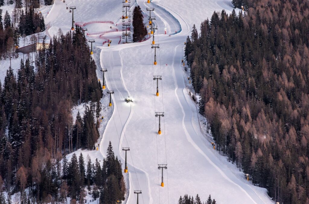 Aerial view of a freshly groomed ski piste winding through snowy forest
